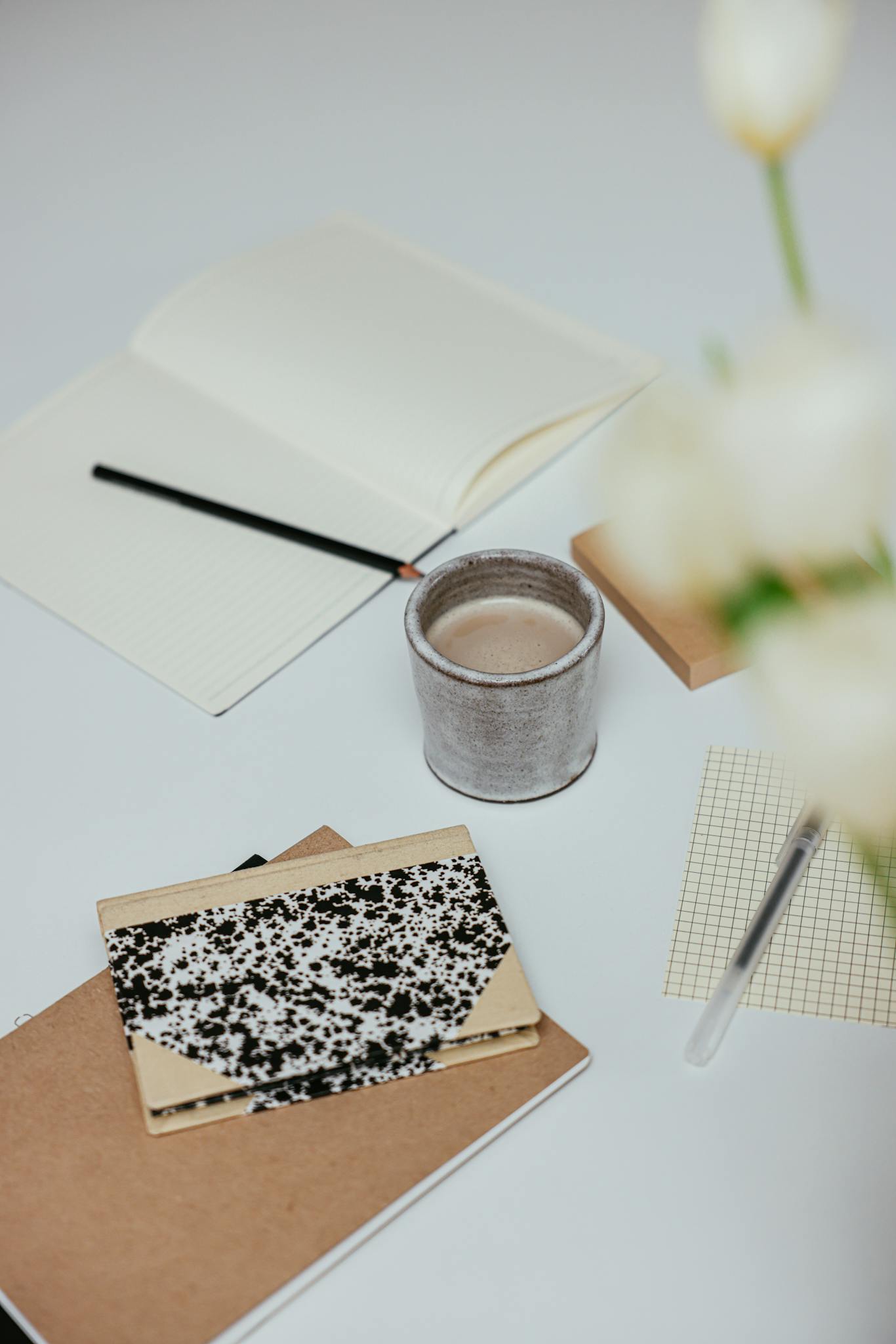 A clean and organized workspace with notebooks, a coffee cup, and stationery on a white surface.