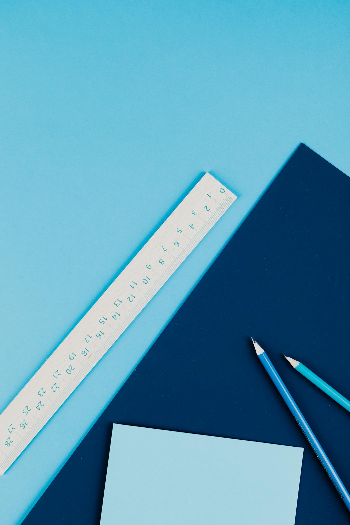 Flat lay of blue toned stationery featuring a ruler and pencils on a blue background.