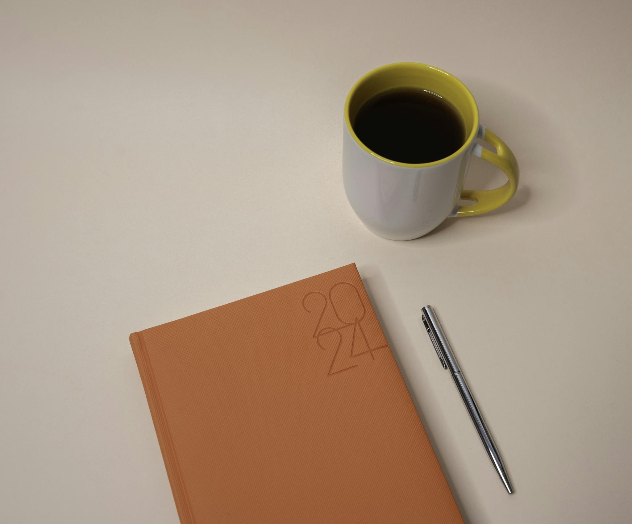 Stylish flat lay of 2024 planner with coffee and pen on a peach background.