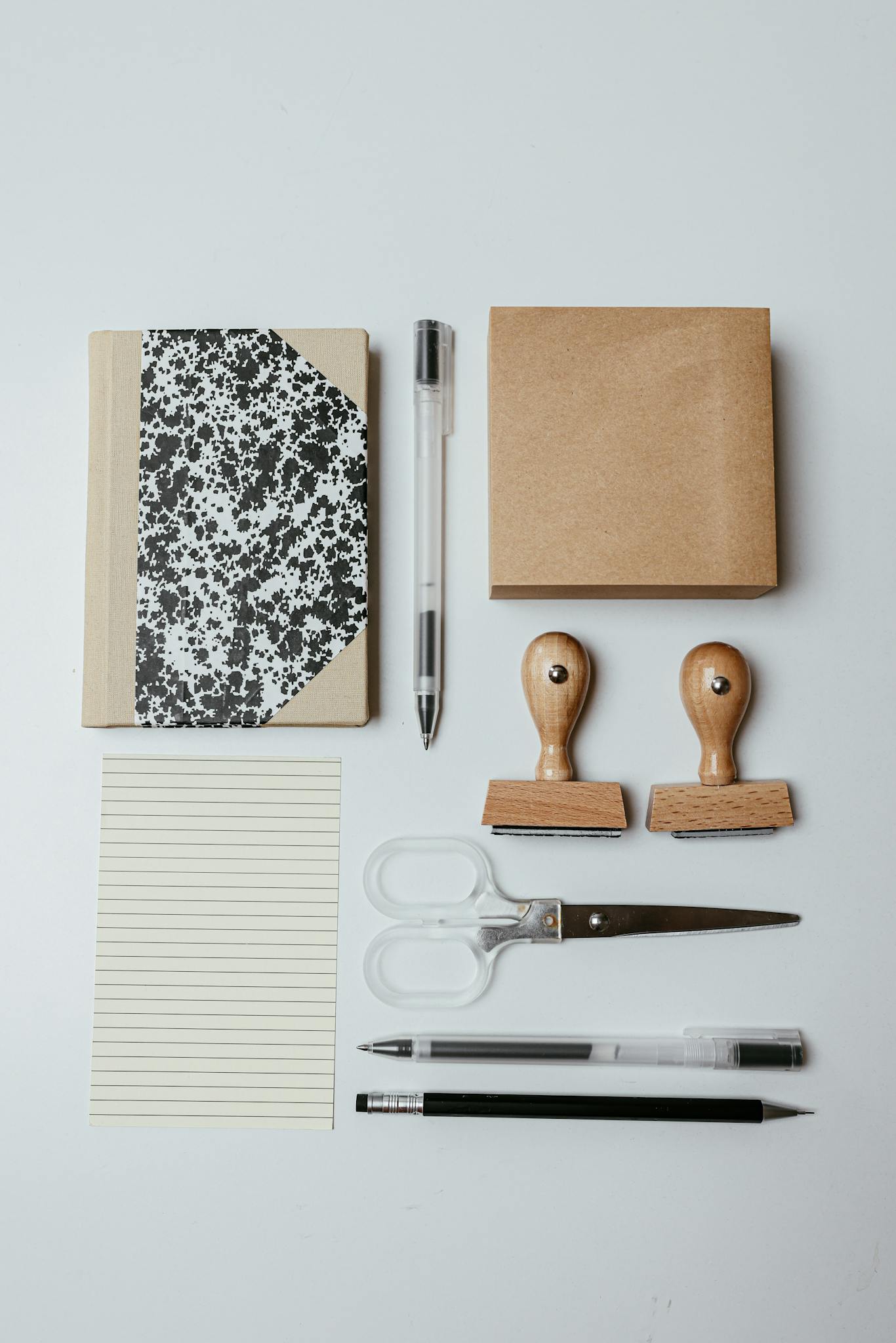 Top view of neatly arranged office supplies including notepad, pens, and stamps on white background.